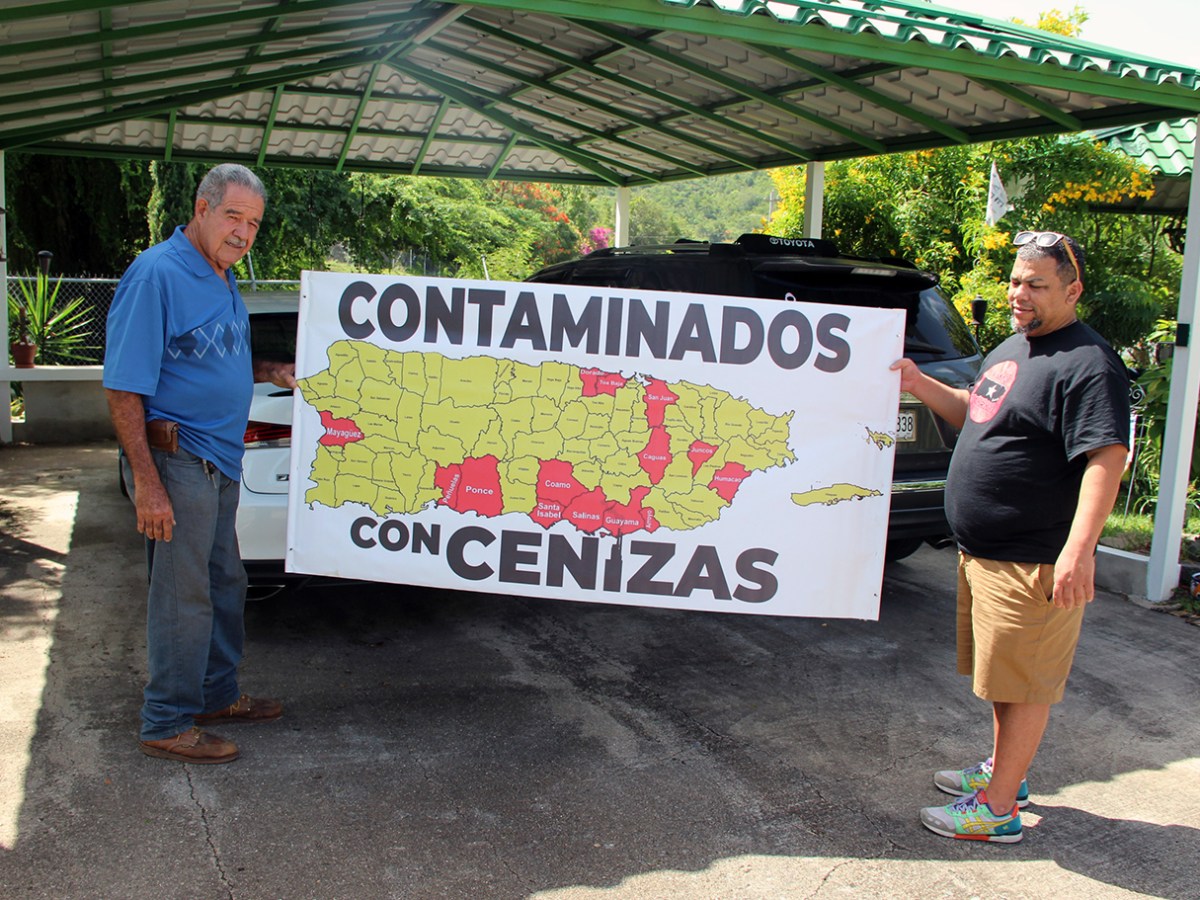 José Cora and Carlos Lago, in fellow activist Sol Piñeiro’s yard, hold a banner showing the parts of Puerto Rico where coal ash has been dumped as construction fill.