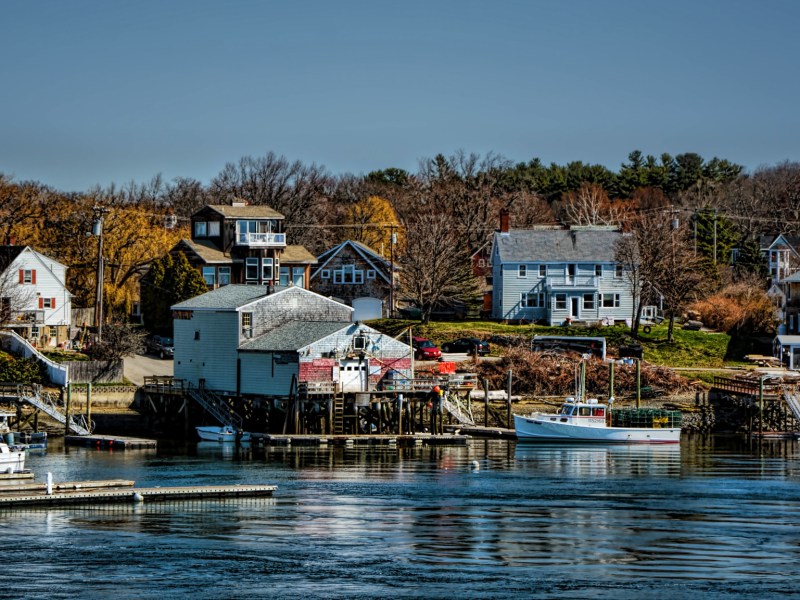 Homes line the rocky coast of Kittery, Maine. Two boats and docks are also visible.