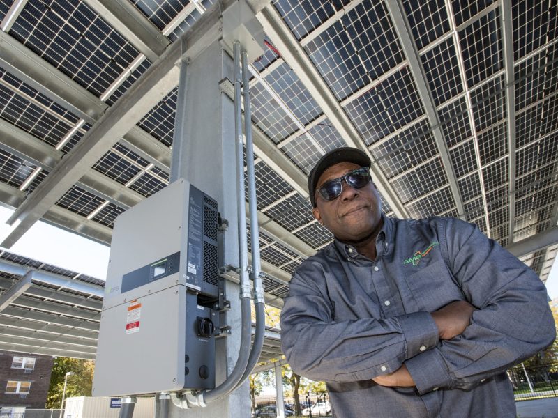 Arthur Burton poses with solar panels and electric vehicle charging stations in the Urban League parking lot.
