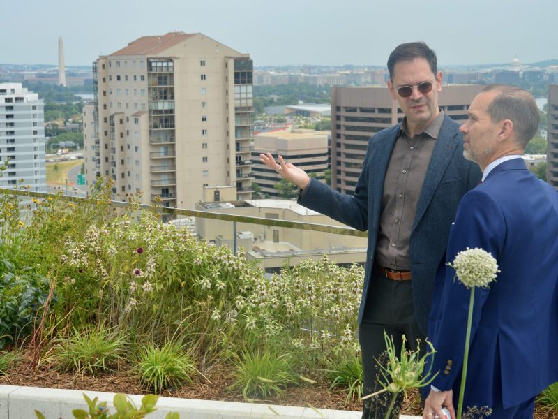 Fernando Arias, left, director of sustainability at Clark Construction, stands near the urban farm featured on the 15th floor terrace at Amazon HQ2. The Potomac River and Washington D.C. landmarks are visible in the background.
