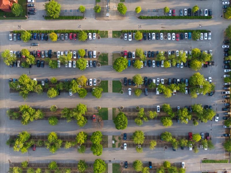 An aerial view of a half-empty parking lot, accented by trees.