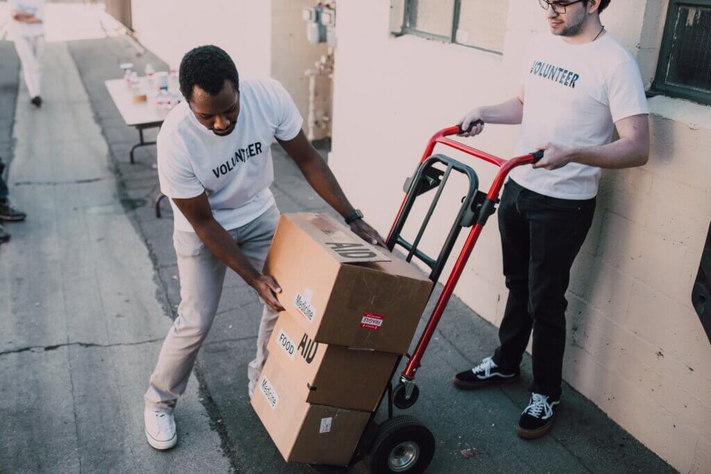 Two volunteers moving boxes with a dolly.