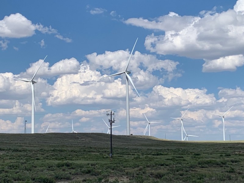 Several large wind turbines line a green hill in Wyoming