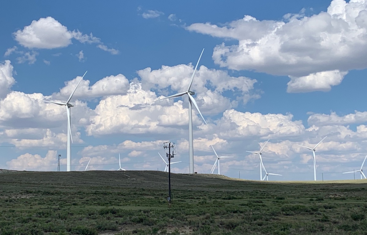 Several large wind turbines line a green hill in Wyoming